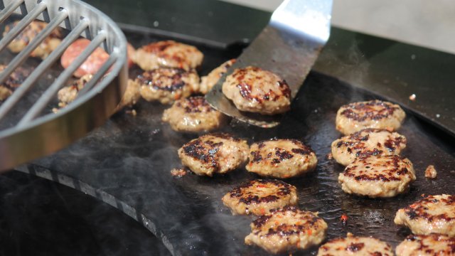 Kleine Hamburger werden mit Grillschaufel auf der Grillfläche des swissfirecube garden gewendet